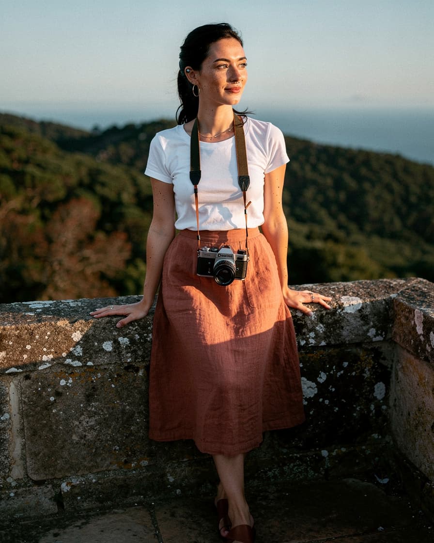 Woman standing on the stone ramparts of the Moorish Castle in Sintra, warm side-light on her face, forested hills and faint ocean horizon behind her.