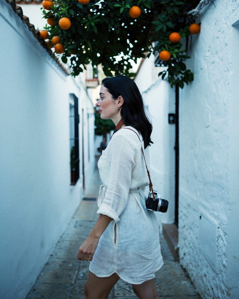 Narrow white-walled alley in Barrio Santa Cruz Seville with orange trees casting shadows in cool early morning light, no people visible.