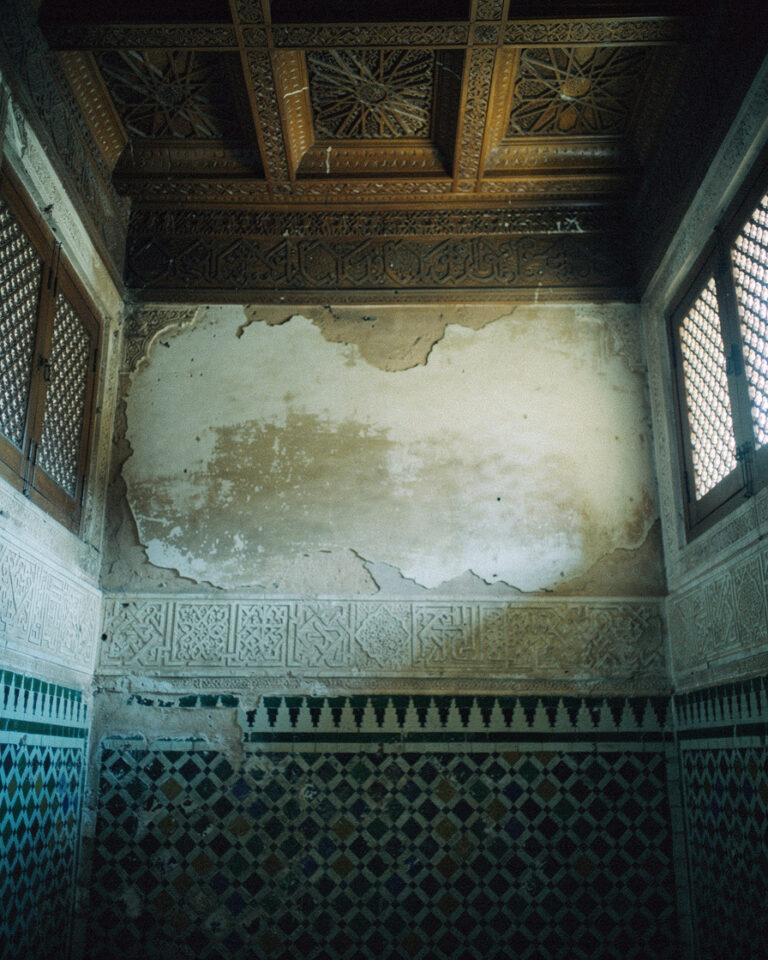 Intricate carved cedar ceiling and geometric zellige tilework inside Bahia Palace in Marrakech, soft morning light filtering through latticed wooden screens.