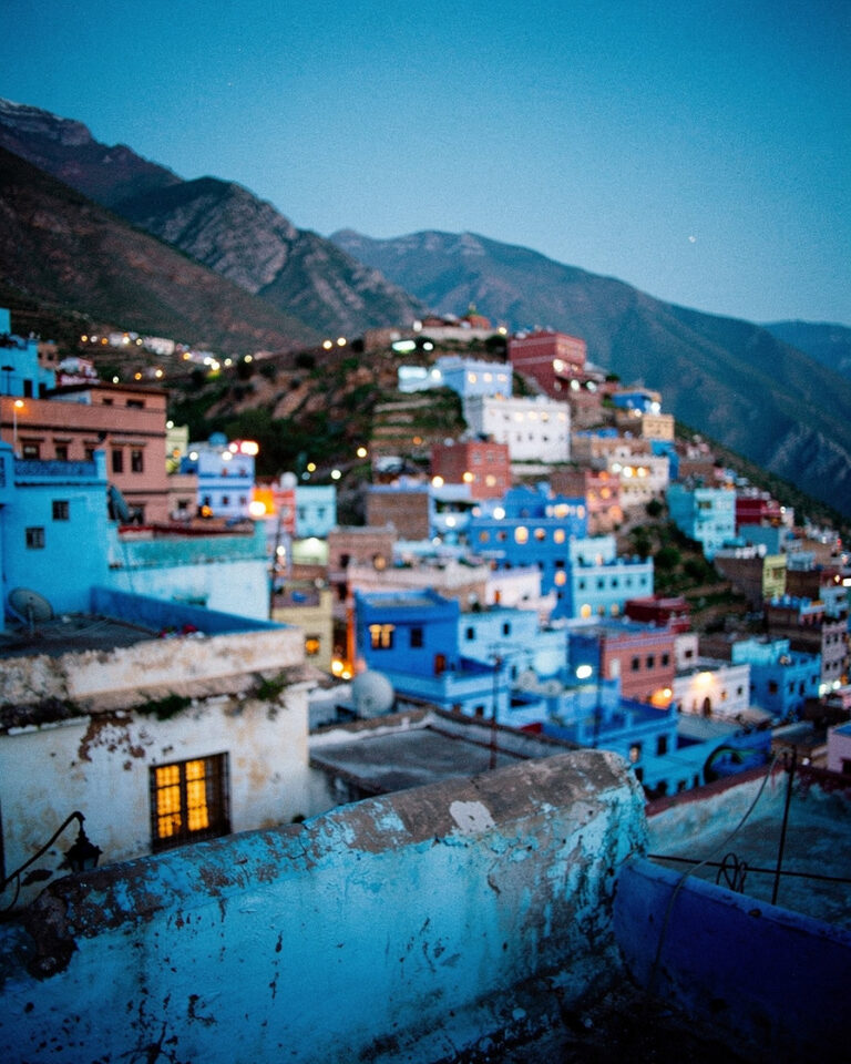 Blue rooftops of Chefchaouen cascading down the Rif mountainside at sunset, warm golden light fading over the blue-washed town, no people in frame.