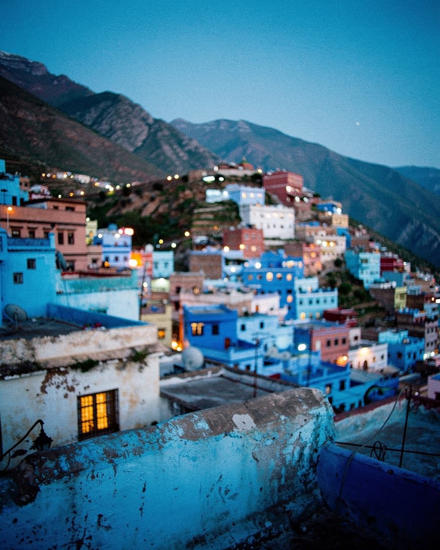 Blue rooftops of Chefchaouen cascading down the Rif mountainside at sunset, warm golden light fading over the blue-washed town, no people in frame.