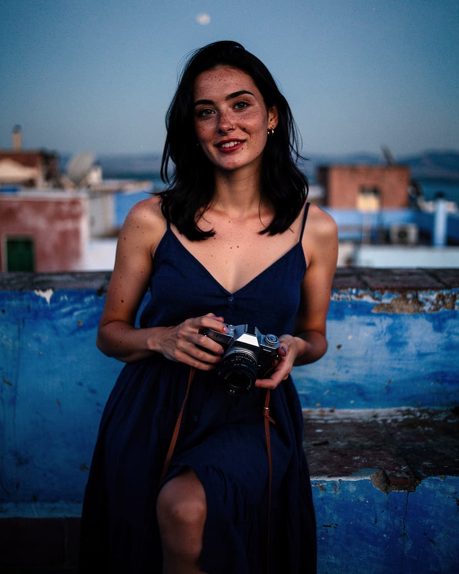 Blue rooftop terrace in Chefchaouen at dusk with a glass of mint tea on a small table, navy-blue walls fading into the Rif mountain valley behind.