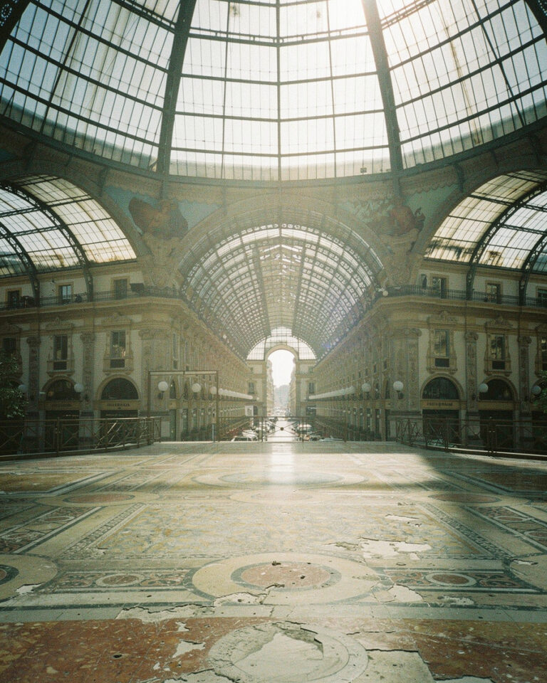 Glass-and-iron vaulted ceiling of Galleria Vittorio Emanuele II in Milan, ornate mosaic floor with no people, soft morning light filtering through the central cupola.