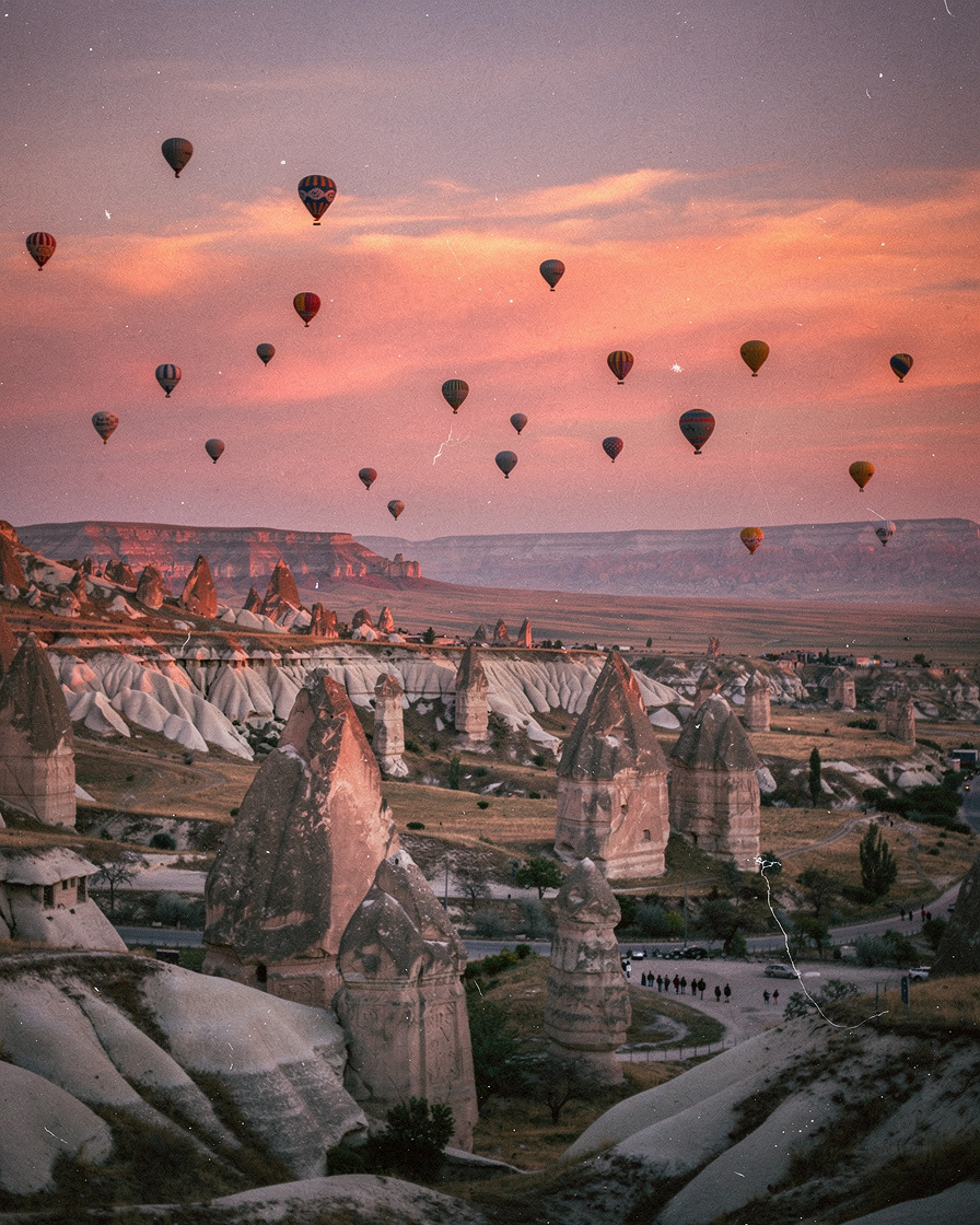 cappadocia hot air balloons: Dozens of hot air balloons drifting over Cappadocia's fairy chimney rock formations at dawn, cor
